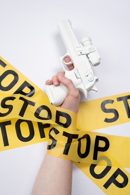Pistola softair bianca in mano avvolta da nastro segnaletico STOP, simbolo di pericolo e allarme, in riferimento all'articolo su Bergamo Alta.