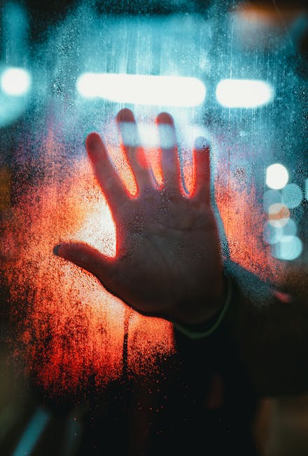 Mano su vetro appannato con luci, metafora della diagnosi e classificazione ICD-10 nella sanità globale.