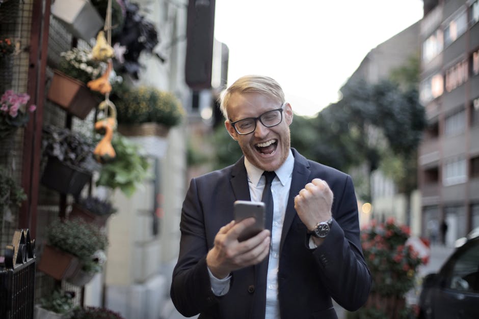 Uomo in giacca esulta guardando il telefono, successo ripetizioni online, risultati positivi, guadagni extra, tutor online soddisfatto