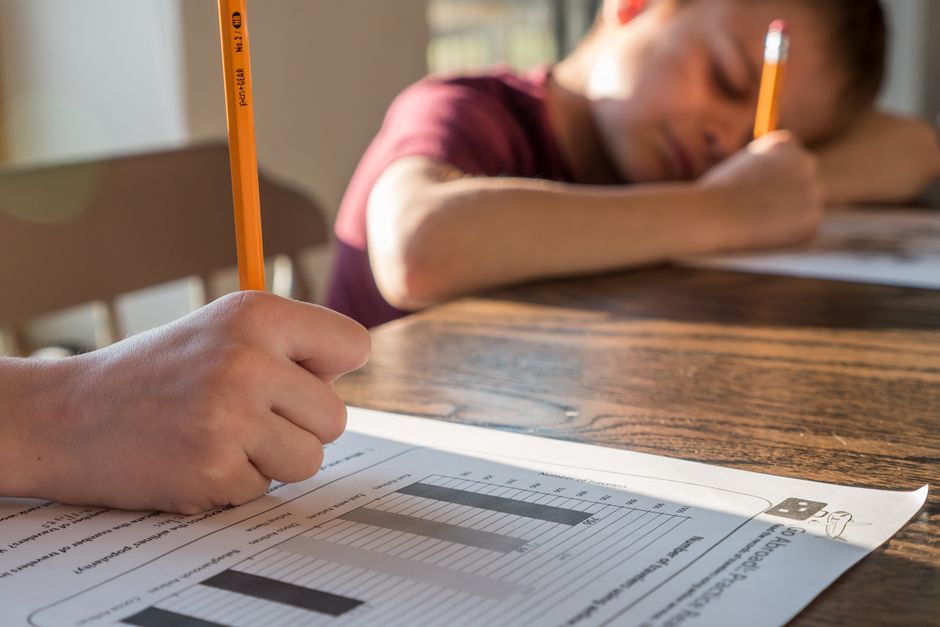 Bambini che studiano con un foglio di esercizi e grafici, uno dei quali sembra esausto, riflettendo sulla dispersione scolastica e la qualità degli apprendimenti secondo i dati INVALSI 2026.