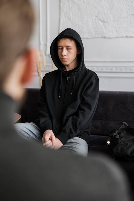 Adolescente con cappuccio in seduta durante una sessione di terapia, focus sulla salute mentale infantile e intervento precoce