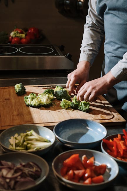 Chef professionista taglia broccoli freschi su tagliere in legno, circondato da ingredienti colorati per una cucina di successo