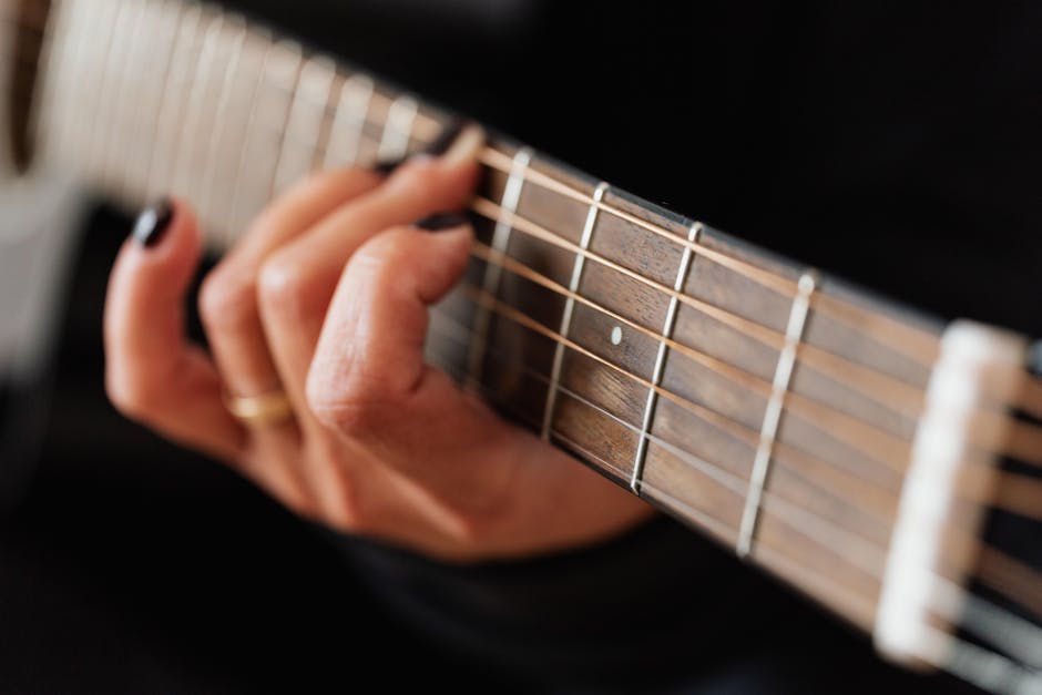 Mano femminile che suona la chitarra acustica, tecnica e passione per la musica in armonia, focus sul manico e le corde.