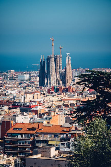 Panoramica aerea della Sagrada Familia di Antoni Gaudí a Barcellona, Spagna, con skyline urbano e mare sullo sfondo.