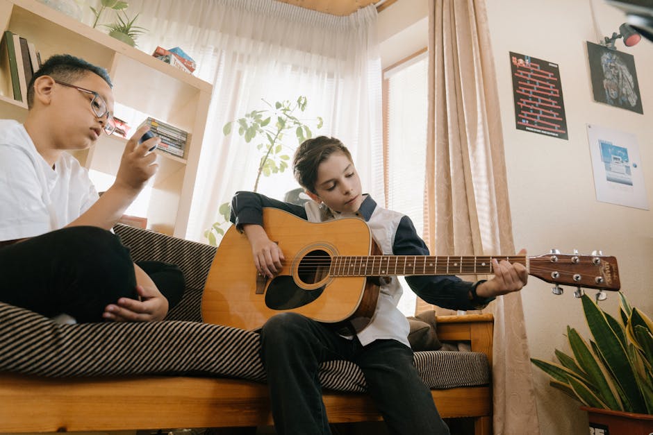 Ragazzo che suona la chitarra acustica mentre un altro usa il cellulare, esempio di educazione musicale e crescita armonica.