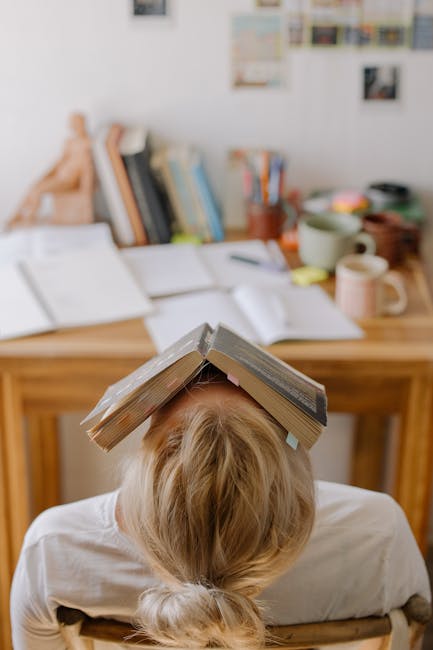 Studente esausto con libri sulla testa, simbolo del perfezionismo scolastico e stress da studio eccessivo. Ricerca finlandese sul tema.