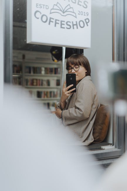 Donna con occhiali legge sul telefono in libreria, riflesso della cultura latina nei conte letterari, approfondimento sulla grandezza letteraria.