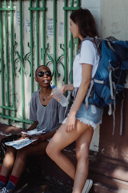 Due amiche viaggiatrici pianificano il percorso con mappa e acqua, simbolo di ACSE Scafati che supporta la comunità locale.