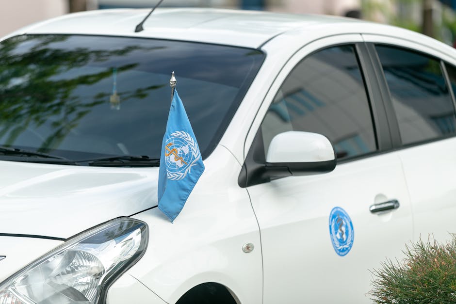 Auto bianca con bandiera dell'Organizzazione Mondiale della Sanità sul cofano, simbolo del ruolo cruciale nella salute globale.