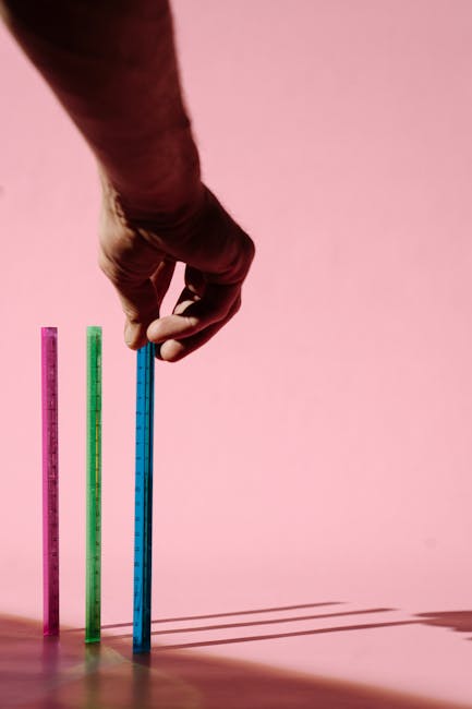 Calcolo altezza figlio: mano misura righelli colorati su sfondo rosa per predire la crescita del bambino