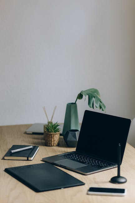 Scrivania ergonomica con laptop, tavoletta grafica, blocco note e accessori per un ambiente di lavoro confortevole e produttivo.