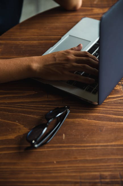 Persona che compila la domanda per il programma Itaca 2025 al computer, con occhiali da vista sul tavolo di legno.