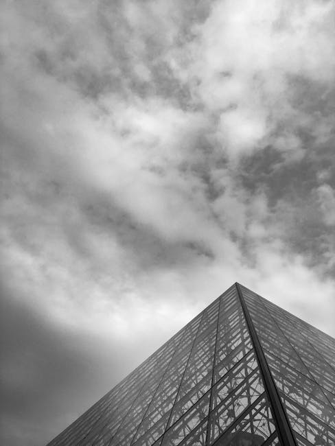 Piramide triangolare regolare in vetro e acciaio contro cielo nuvoloso, esempio di eleganza geometrica e design architettonico moderno.