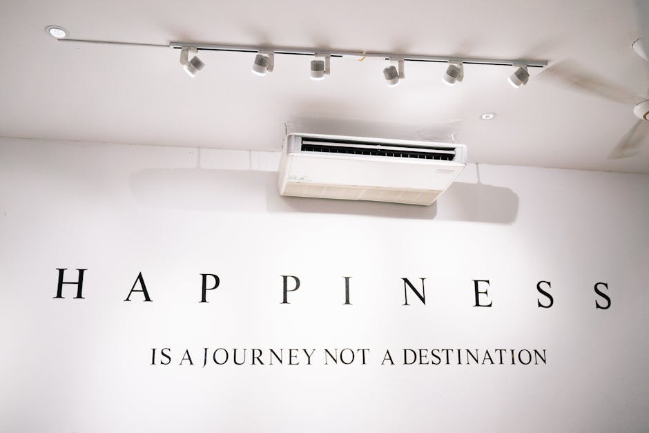 Scritta Happiness is a journey not a destination su muro bianco, riflessioni sulla vita e il pensiero di Moravia, illuminazione a faretti.