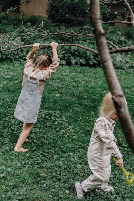 Due bambine giocano all'aperto con rami e una pala, attività ludiche per lo sviluppo motorio e la coordinazione nei giochi ritmici.