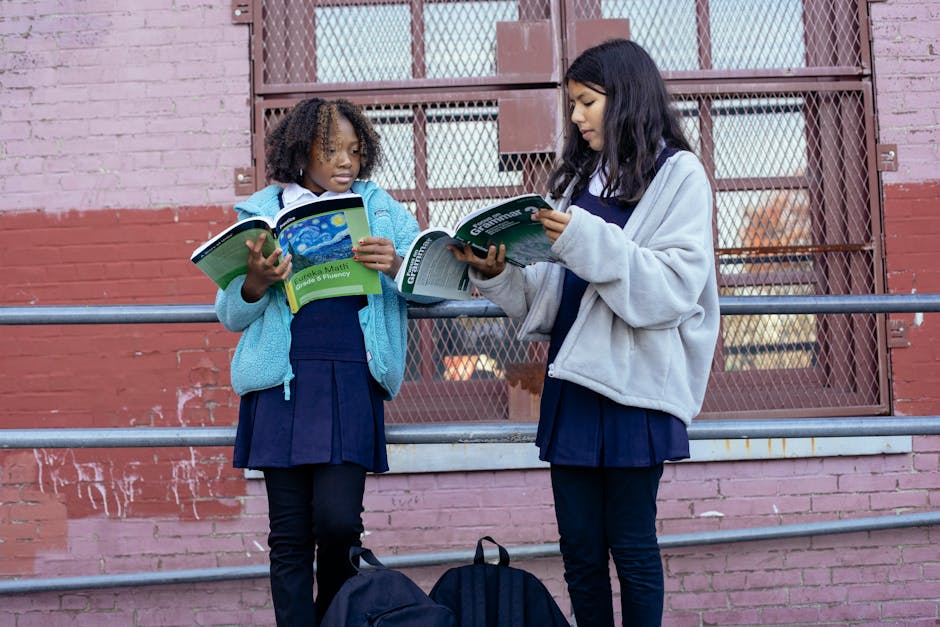 Due studentesse elementari ripassano i compiti di matematica e grammatica all'aperto, zaini appoggiati a terra. Guida per genitori.