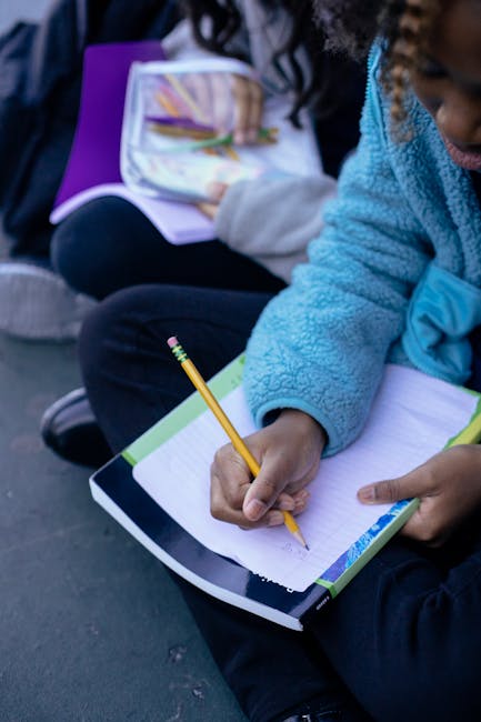 Ragazza scrive su quaderno con matita, focus sull'importanza della scrittura a scuola e l'apertura mentale promossa dalla lettura.