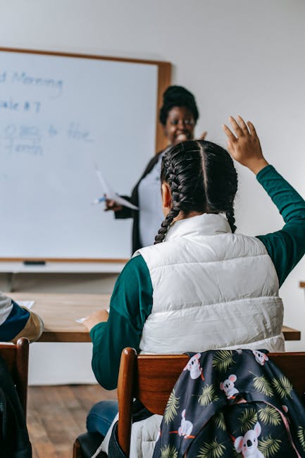 Studentessa alza la mano in classe durante la lezione di italiano, assistente di lingua italiana all'estero in secondo piano. Bando a.s. 2026/2027.