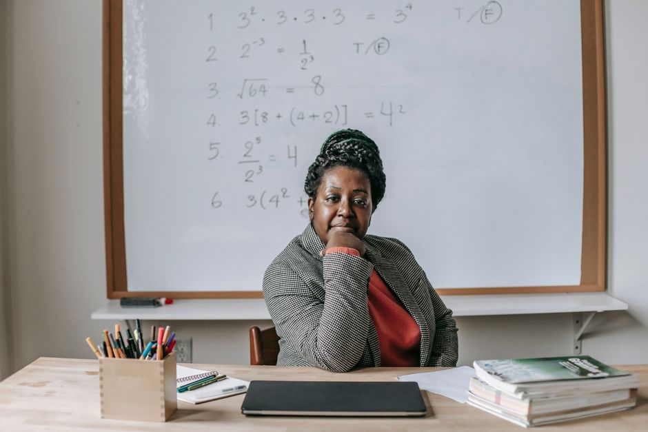 Insegnante di matematica con espressione pensierosa davanti a una lavagna con esercizi, simbolo di autorevolezza scolastica e riflessione sulle aggressioni.