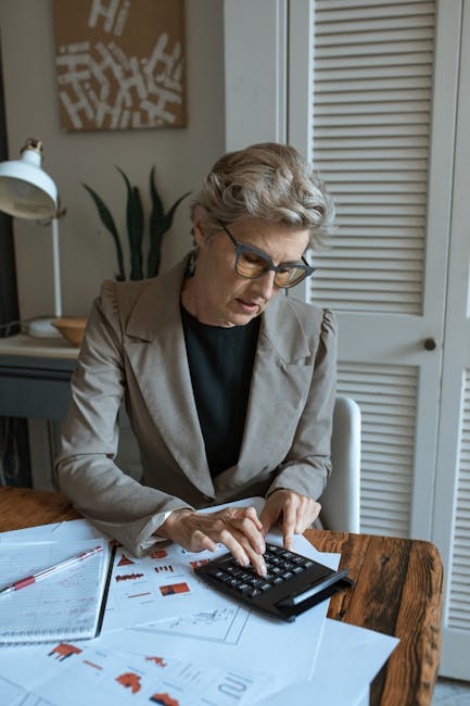 Donna che usa calcolatrice per calcolare percentuali su documenti finanziari, semplificando la gestione delle finanze personali e aziendali.