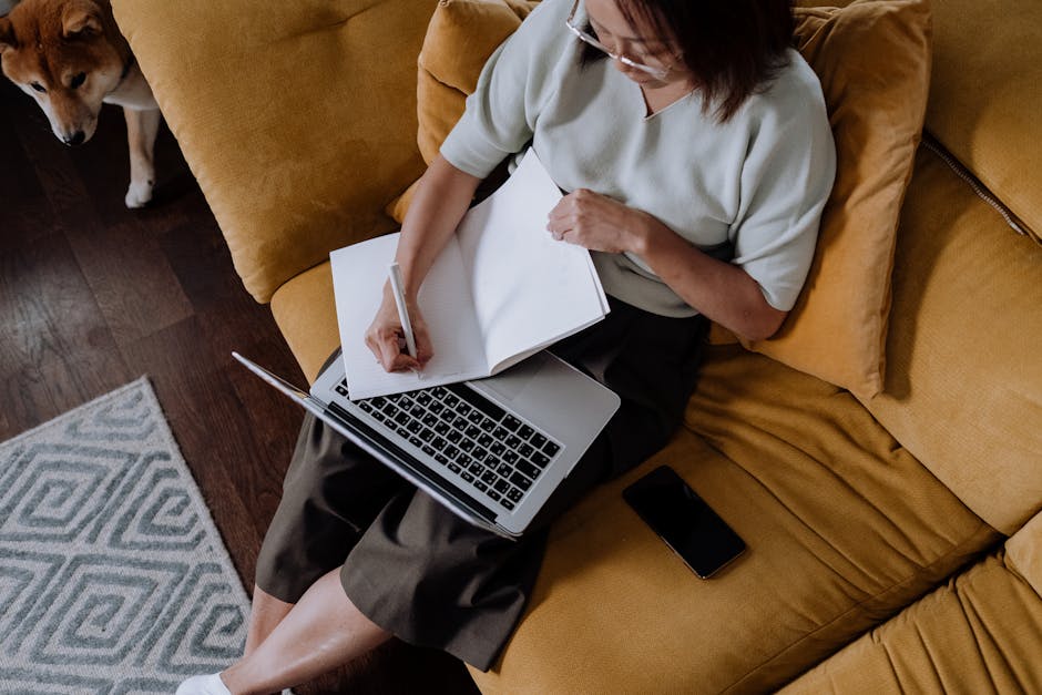Donna studia con laptop e quaderno su divano giallo, cane Shiba Inu sullo sfondo. Preparazione all'evento sull'uso consapevole dell'IA.