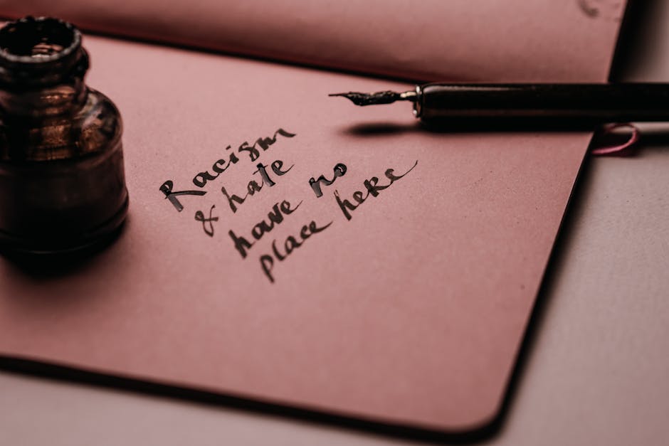 Calligrafia su carta rosa con frase 'Il razzismo e l'odio non hanno posto qui', simbolo dell'impegno contro l'antisemitismo e l'odio razziale.
