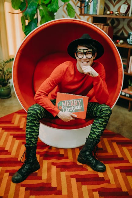 Uomo sorridente seduto in poltrona rossa con occhiali Happy New Year e libro Merry Christmas, musica per benessere festivo.