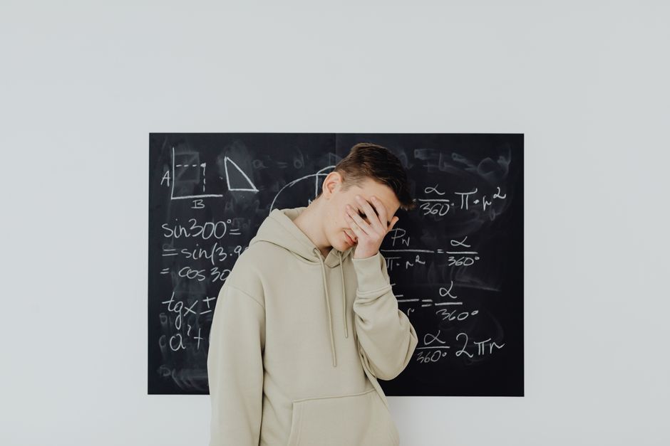 Studente con espressione frustrata davanti a una lavagna con formule matematiche, simbolo di bocciatura per insufficienza e discalculia