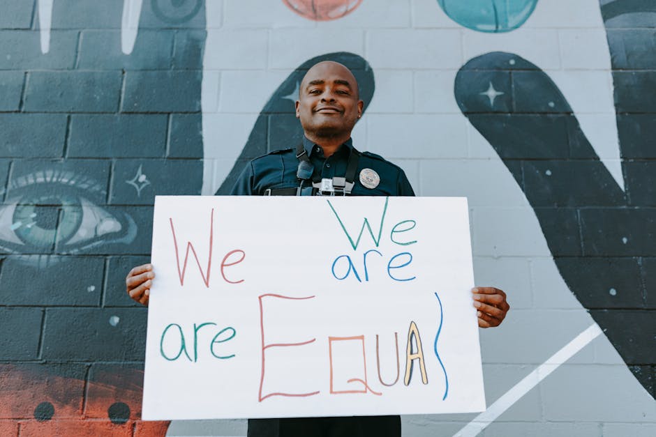 Agente di polizia afroamericano sorridente con cartello 'We are Equal' per inclusione e trasformazione sociale