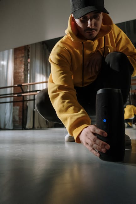 Uomo con felpa gialla interagisce con speaker Bluetooth nero, promuovendo attività musicali stimolanti e il potere della musica.