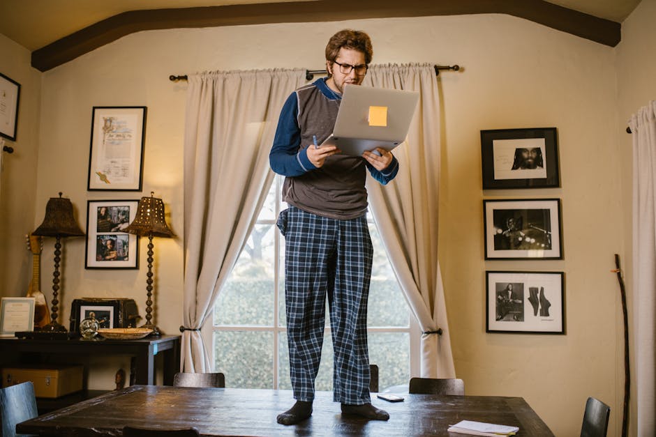 Uomo in pigiama lavora su un laptop in piedi su un tavolo, esempio di approccio innovativo alla pedagogia digitale e apprendimento flessibile.