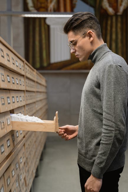 Uomo consulta schedario in archivio, esempio di Sistema di Classificazione Unico per organizzare e trovare informazioni velocemente.