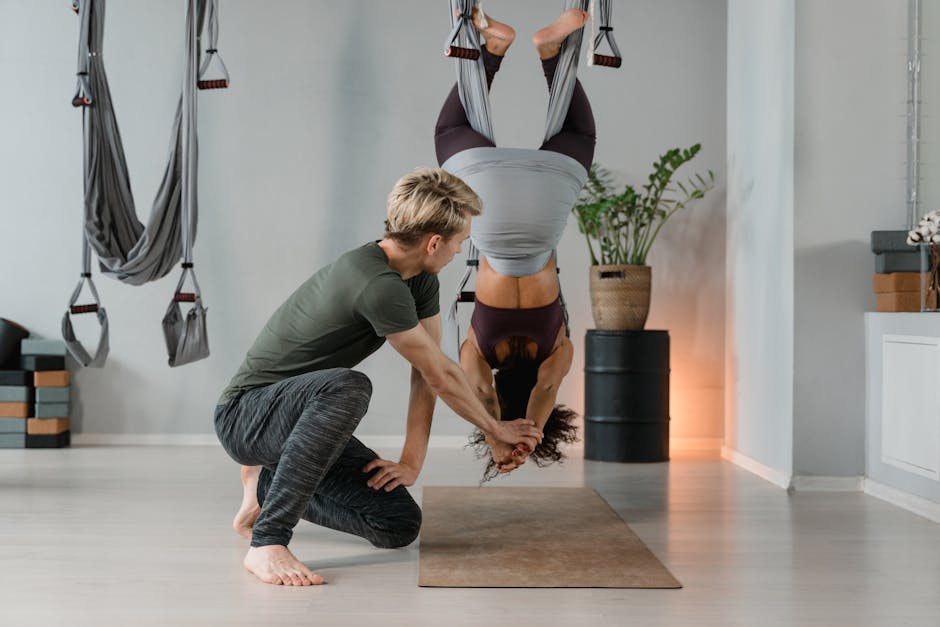 Istruttore assiste studentessa durante esercizio di yoga aereo per la gestione dello stress e la resilienza scolastica.