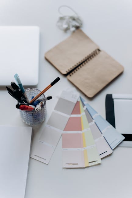 Scrivania con quaderno aperto, campioni colore, penne e laptop: metafora visiva per il declino delle capacità di scrittura nei giovani.