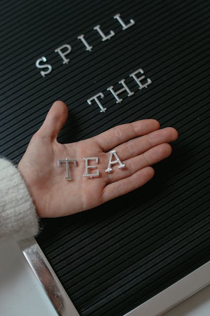 Mano che tiene le lettere TEA su una lavagna con la scritta Spill the Tea, metafora della grammatica italiana rivelatrice.