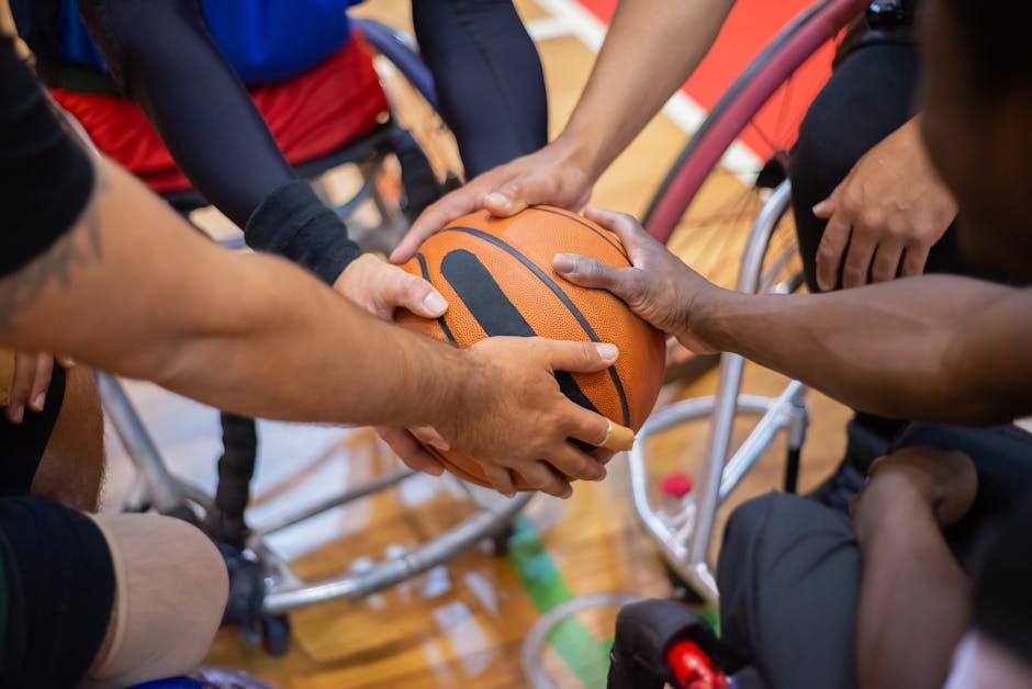 Inclusione scolastica e sport: mani di atleti in carrozzina che si passano una palla da basket, simbolo di collaborazione e superamento delle disabilità sensoriali.