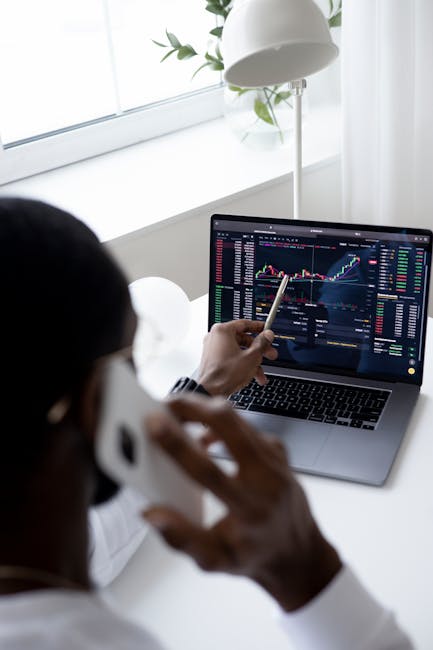Uomo al telefono che analizza grafici finanziari su laptop, monitorando l'andamento dei contagi per valutare l'impatto del morbillo a Londra.