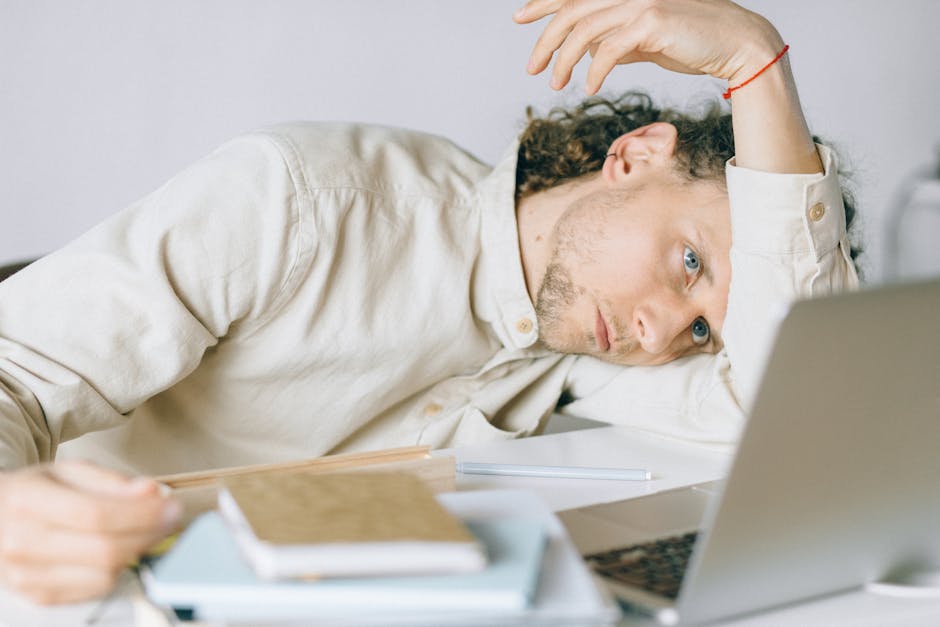 Uomo esausto appoggiato alla scrivania con laptop, simbolo di affaticamento da AI e sovraccarico mentale legato all'uso intensivo dell'intelligenza artificiale.