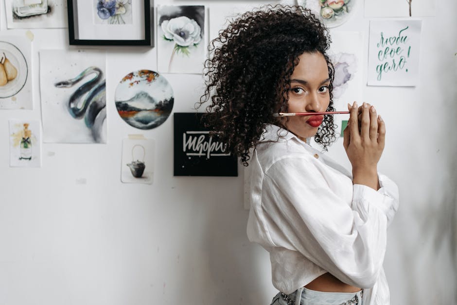 Giovane donna con pennello tra le labbra, ispirazione artistica e creatività, abbigliamento casual, sfondo con dipinti e disegni.