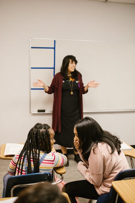 Insegnante spiega un concetto a due studentesse in classe, focus sulla chiarezza delle spiegazioni scolastiche e la riformulazione dei concetti.