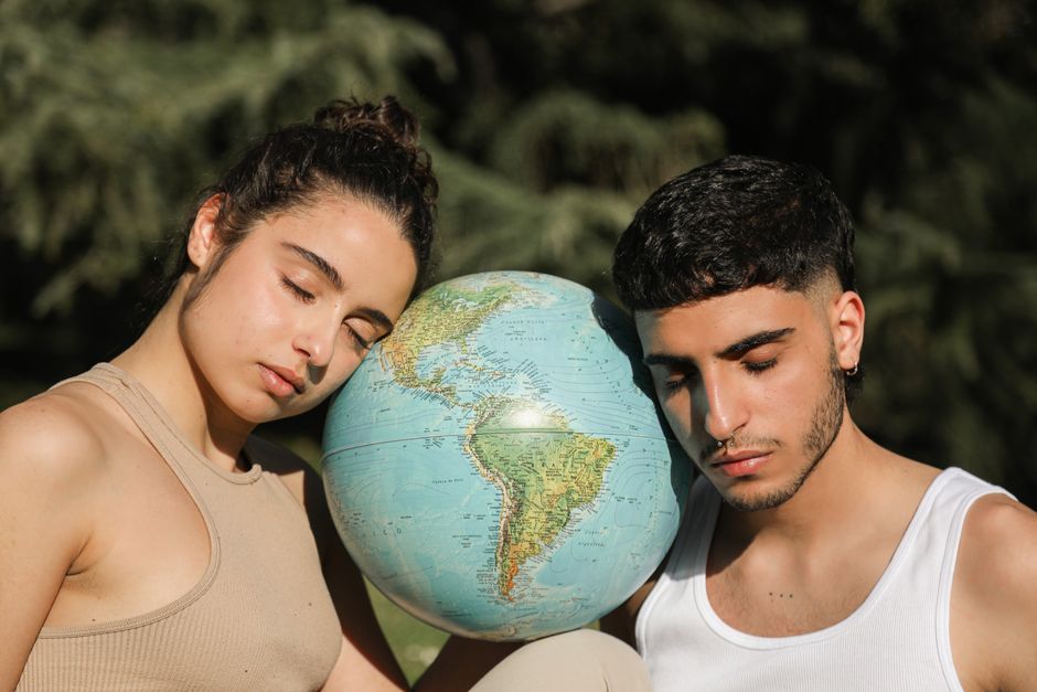 Giovani con gli occhi chiusi appoggiati a un globo terrestre, simbolo delle ansie generazionali e del disagio esistenziale tra geopolitica e futuro.