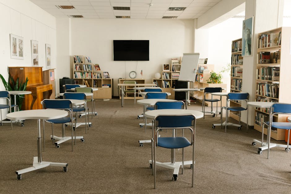 Aula scolastica con tavoli e sedie su rotelle, librerie sullo sfondo, spazio per l'educazione e la formazione cinematografica.