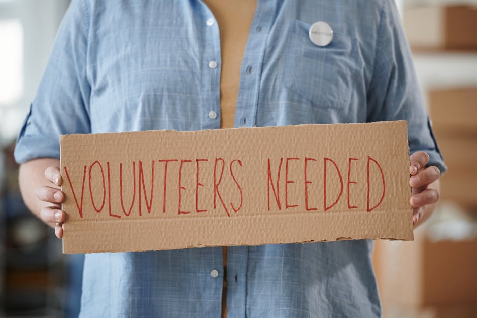 Volontario con cartello 'Volunteers Needed' per bando unico: opportunità di partecipazione e massimizzazione dei risultati