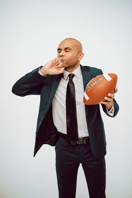 Uomo in giacca e cravatta con pallone da football, metafora di strategia e flessibilità aziendale per il successo.