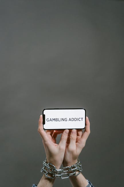 Mani incatenate che mostrano uno smartphone con la scritta Gambling Addict: metafora della dipendenza dal gioco d'azzardo online.