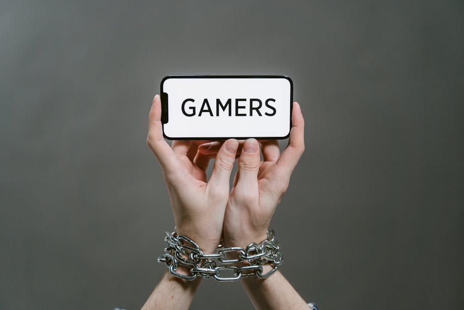 Dipendenza da videogiochi: mani incatenate che sorreggono uno smartphone con la scritta Gamers, simbolo della dipendenza giovanile dai social e dai giochi online.