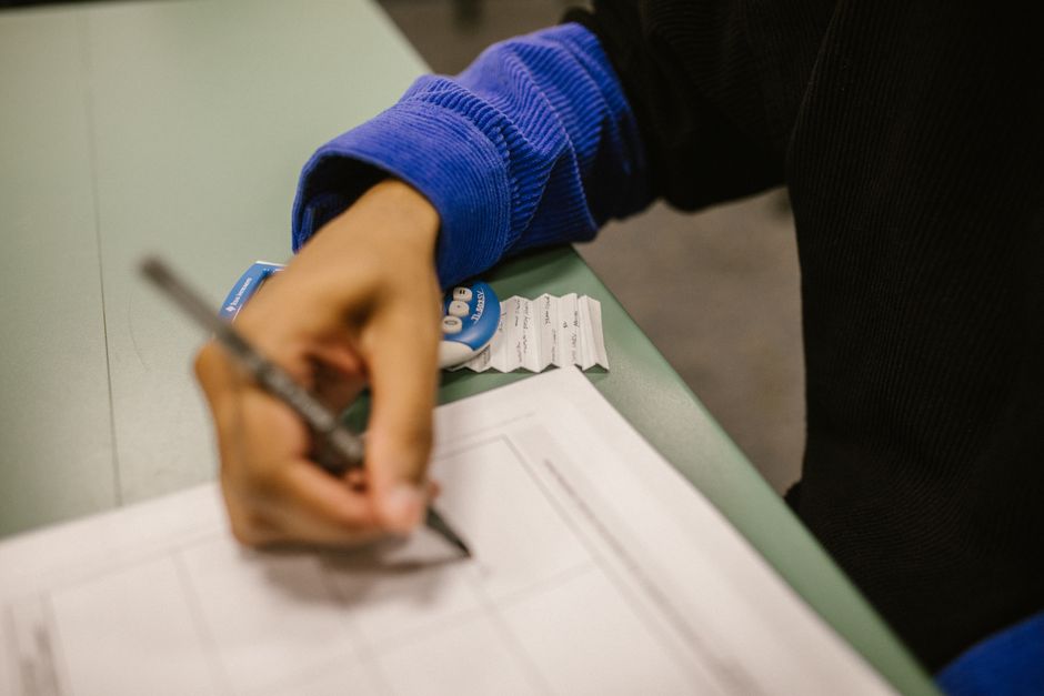 Studente con disabilità che scrive durante una prova equipollente, con foglietti e timer sul banco