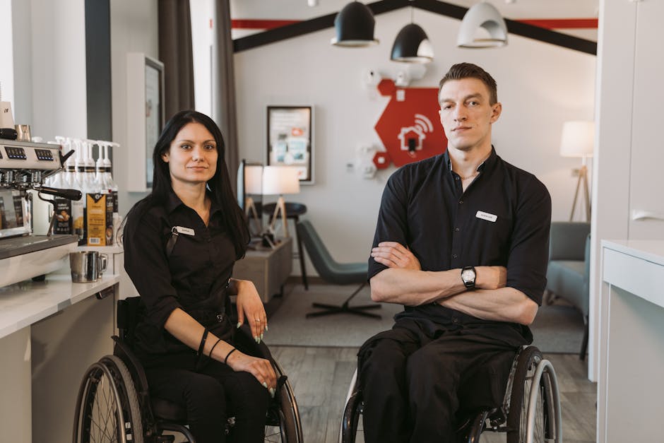 Due persone in sedia a rotelle, sorridenti, in un ambiente lavorativo inclusivo. Tecnologia e accessibilità per prove adattive.