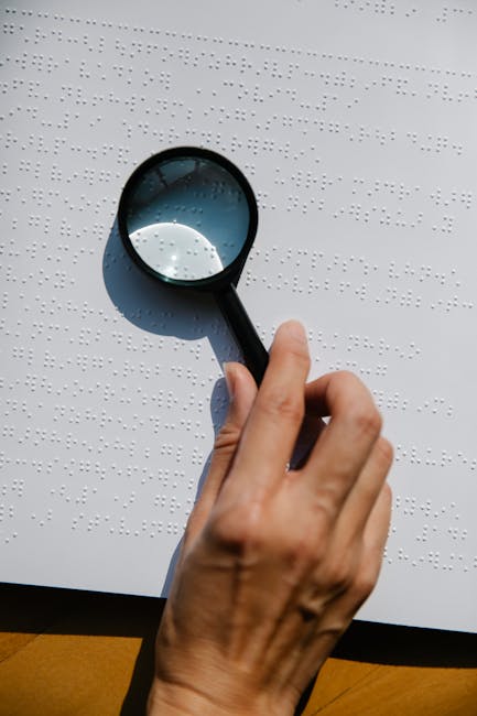 Mano che esplora testo Braille con lente d'ingrandimento, importanza della percezione visiva e tattile nell'educazione inclusiva.