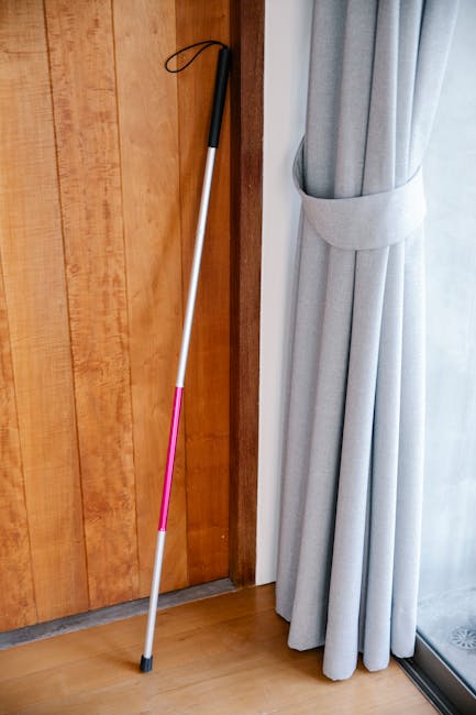 Bastone bianco appoggiato a porta in legno e tenda grigia, utile per calcolare gli spazi e i metri quadri di un ambiente.